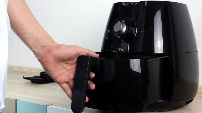 A hand opening an air fryer basket 