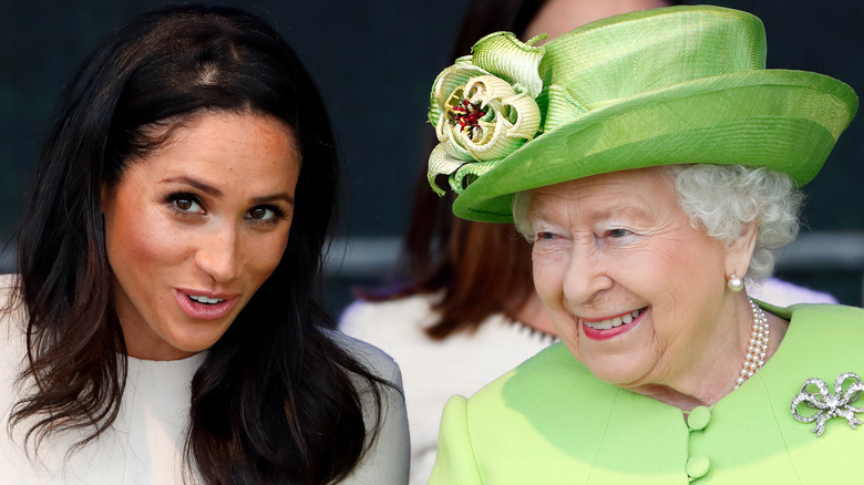 Queen Elizabeth wearing a green suit and hat with Meghan Markle wearing a white dress