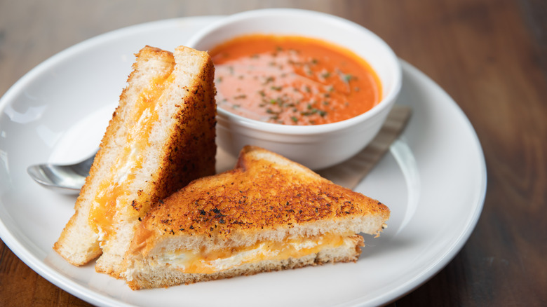 Grilled cheese on white plate with tomato soup in background