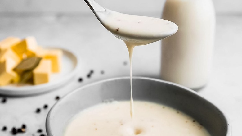 metal spoon dripping bechamel into a bowl