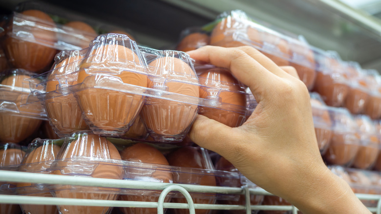 Hand holding package of brown eggs at supermarket