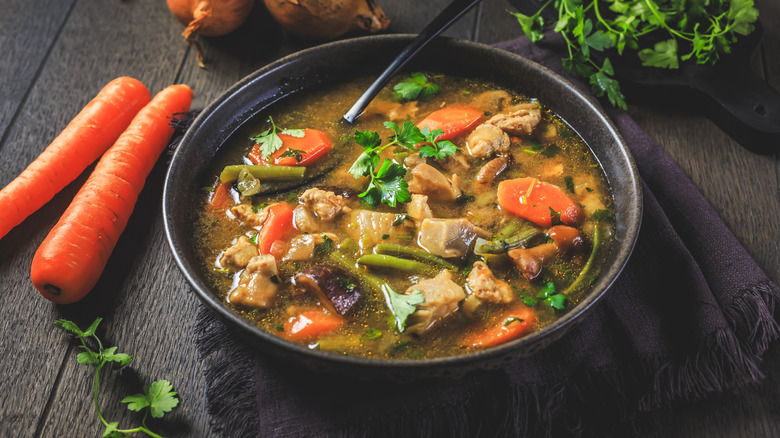 Beef and vegetable soup in bowl with spoon and ingredients spread around