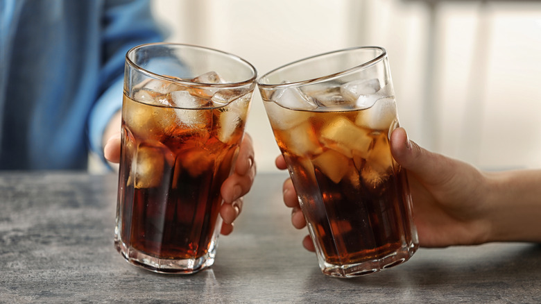 two people cheers with two glasses of cola with ice