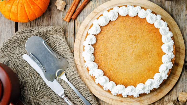 Full pumpkin cheesecake next to serving utensils