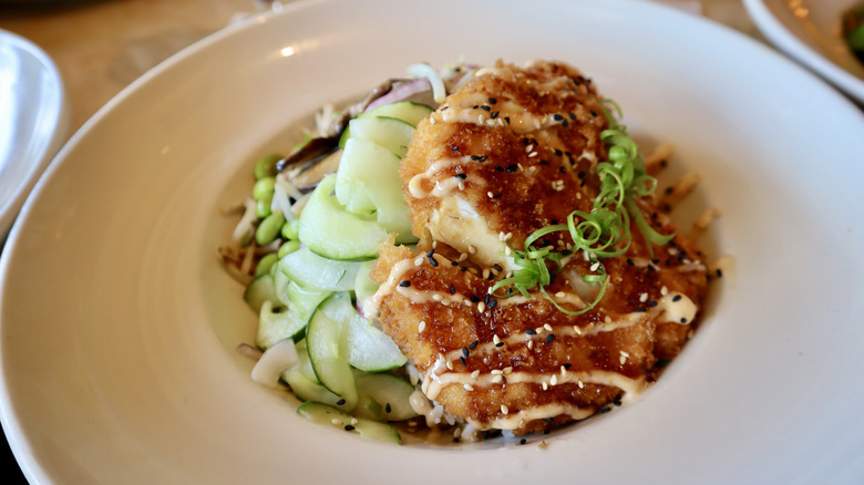 Chicken katsu with sliced cucumbers in white bowl