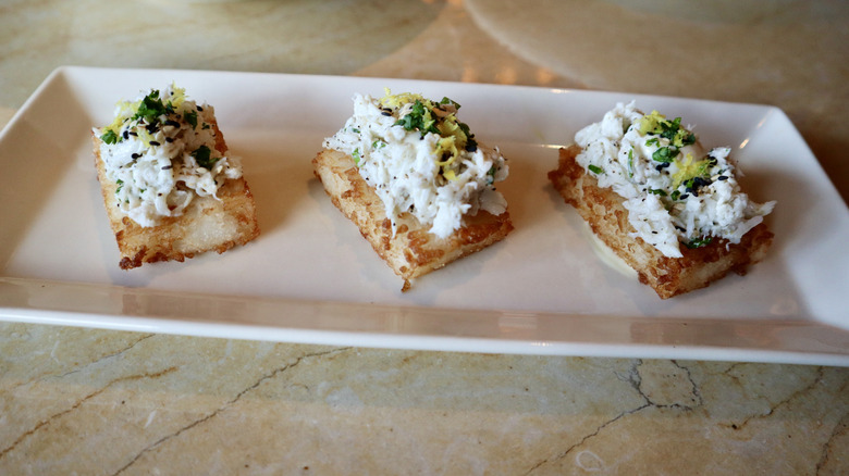 three crispy rice squares topped with crab on white plate