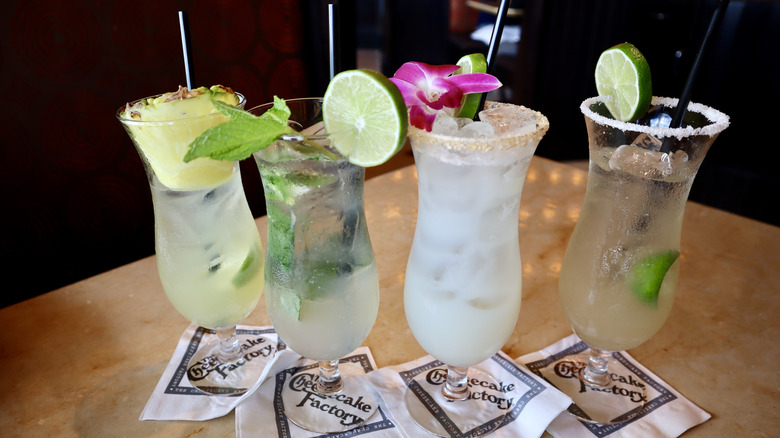 Four bright drinks with fruit garnishes on table