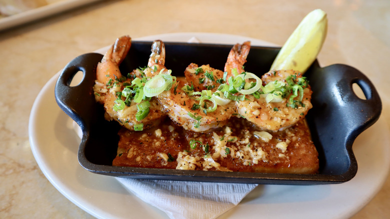 Three shrimp with lemon wedge and sauce in small pan
