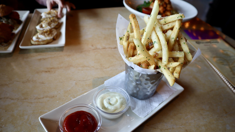 French fries in metal cup on plate with dipping sauces