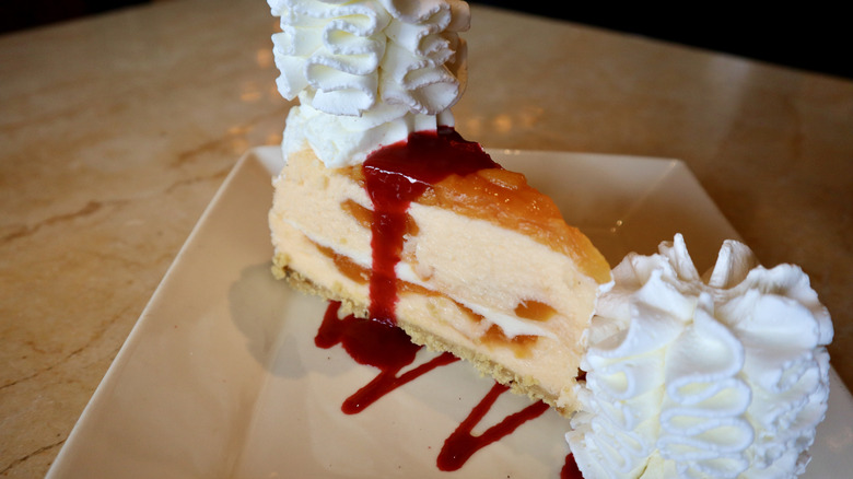 Peach topped cheescake with red sauce and whipped cream on plate