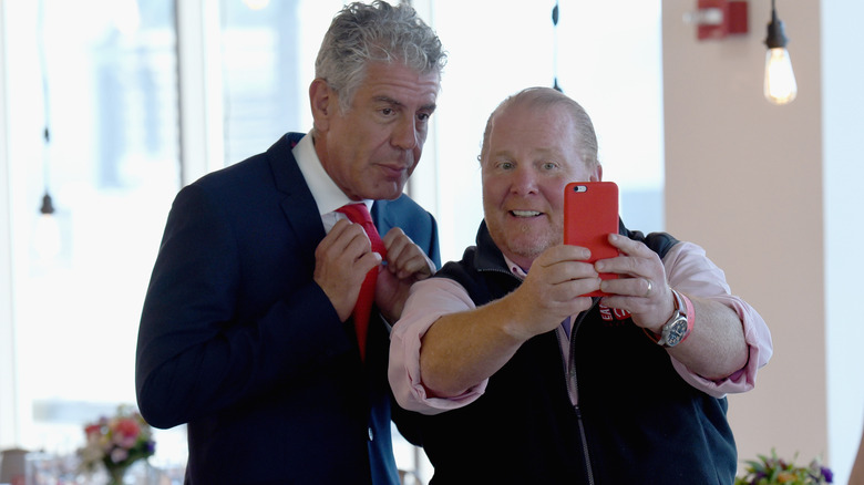 Anthony Bourdain holds his red tie while Mario Batali takes a selfie of them together