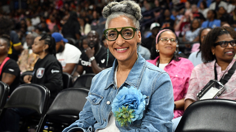 Carla Hall smiles at the camera while sitting in a sporting event