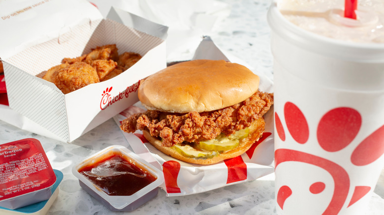 Chicken sandwich, nuggets, beverage, and sauces from Chick-fil-A on table.