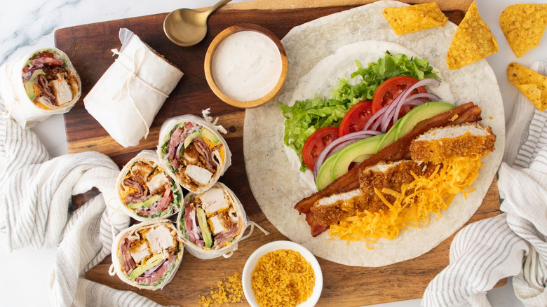 Unwrapped chicken bacon ranch wrap next to halved ones, chips, and bowl of ranch
