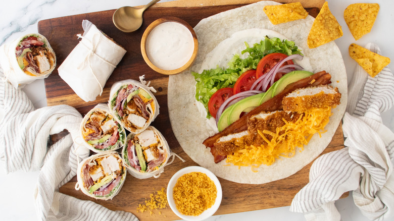 Opened chicken bacon ranch wrap surrounded by wrap halves, chips, and ranch on wooden board