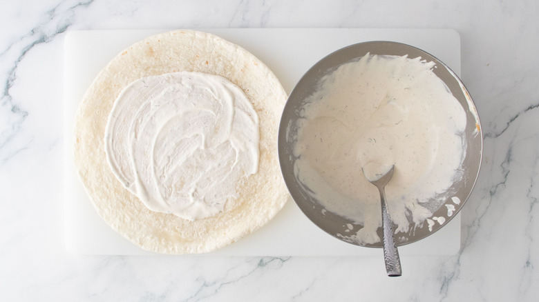 Ranch dressing spread over tortilla next to bowl of ranch