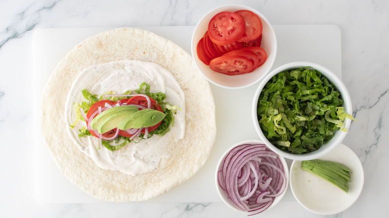 Tortilla topped with ranch and veggies next to bowls of various veggies