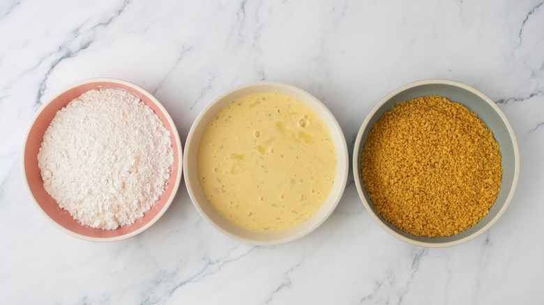 Dredging station with flour in one bowl, beaten eggs in the next, and crushed chip crumbs in the last