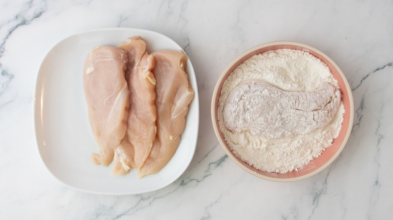 Raw chicken cutlets on plate next to cutlet in flour
