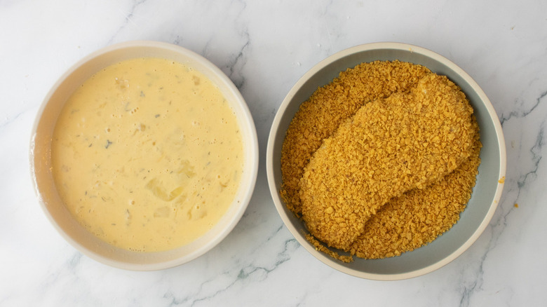Bowl of beaten eggs next to chicken coated in crumbs in separate bowl