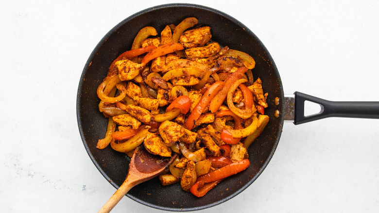 Spicy chicken, peppers, and onions cooking in frying pan