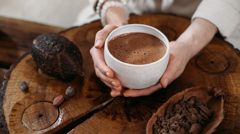 A mug of hot chocolate next to a cacao bean