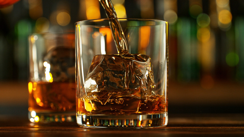 Whiskey being poured into a glass with ice cubes.