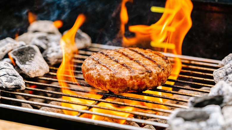 Burger cooking on a grill with flames shooting up around it