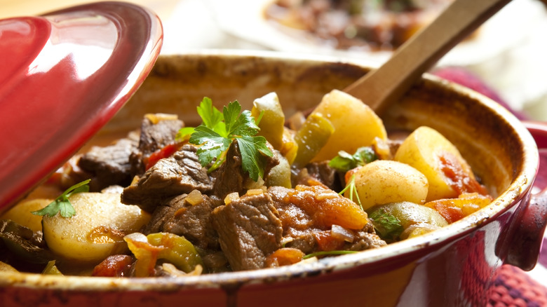 Beef stew in an open red pot with a wooden spoon.