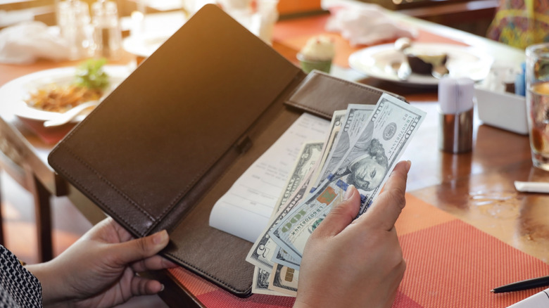 Person settling expensive restaurant check with cash