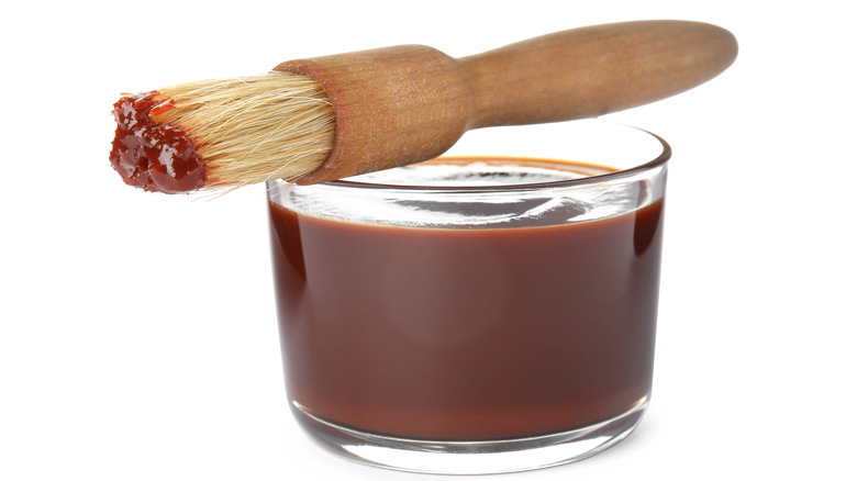 Basting brush setting on top of glass bowl with sauce in it