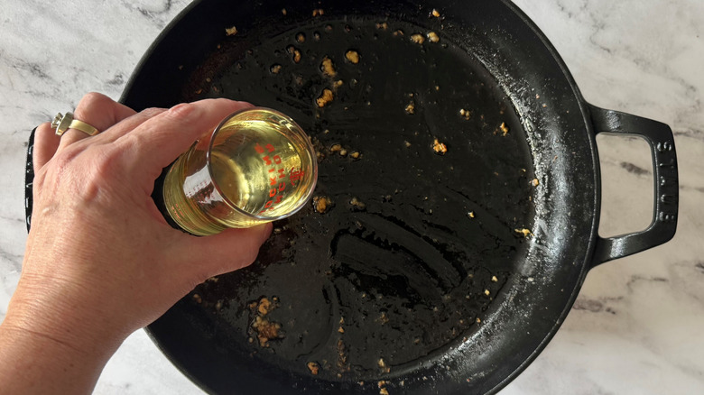 hand holding yellowish liquid above a black pan