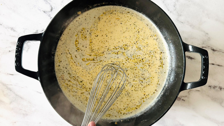 hand holding whisk over beige sauce in a black pan
