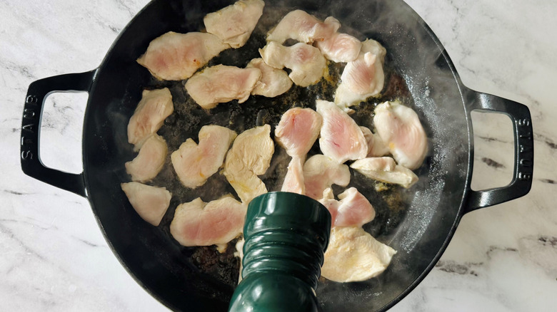 salt or pepper grinder hovering over pan of chicken