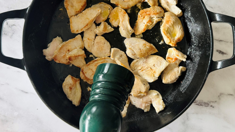 salt or pepper grinder hovering over pan of chicken