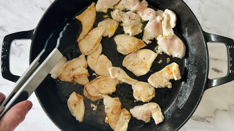 hand using tongs to push chicken around a pan