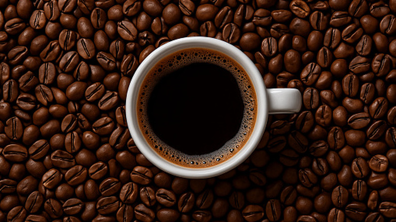 White cup of coffee surrounded by beans