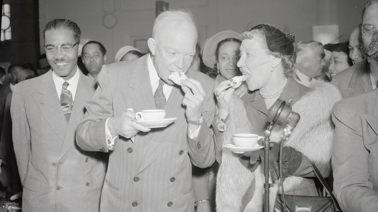 Dwight Eisenhower biting into a baked good while holding cup of coffee