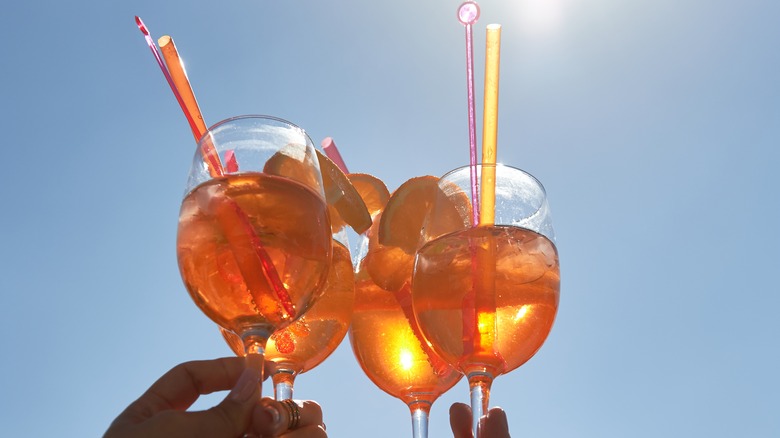 Hands holding orange-hued cocktails up to the light