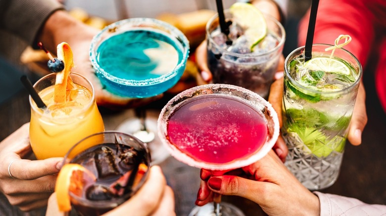 Hand holding a variety of different, brightly-colored cocktails 