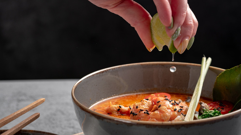 Squeezing lime into broth with shrimp and sesame seeds, and chopsticks in bowl and on the side.