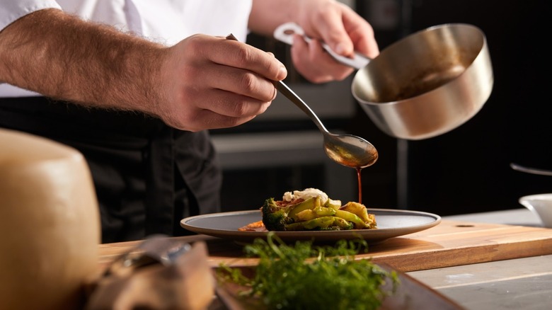 A chef spooning sauce onto a plate