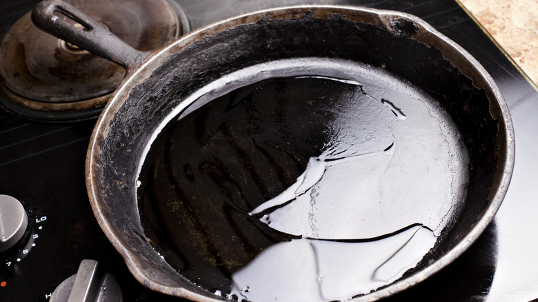 A cast iron skillet with some oil in the center being warmed on a stovetop