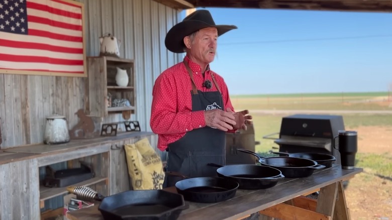 Cowboy Kent Rollins in an outdoor set doing a demonstration with five cast iron skillets on a table