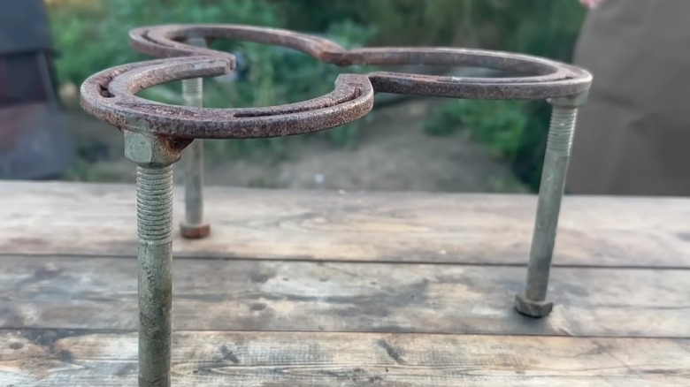 A horseshoe trivet with three legs designed by Cowboy Kent Rollins standing on wooden surface