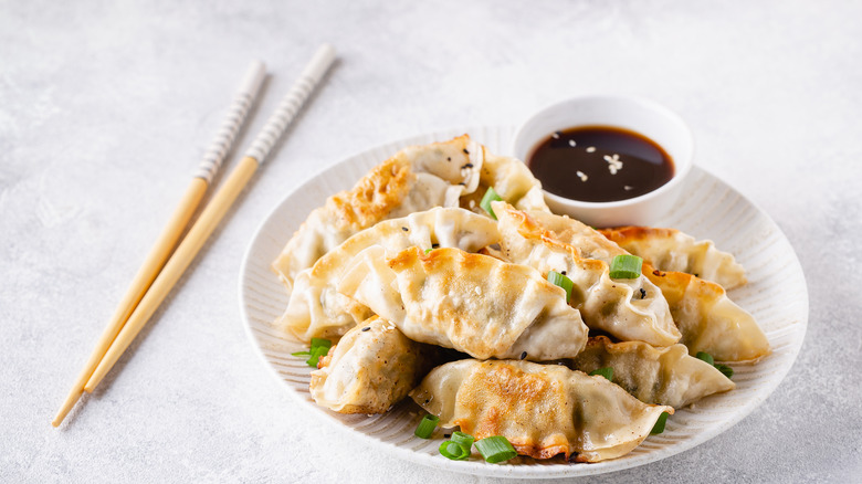 A plate of fried dumplings with soy sauce in the middle