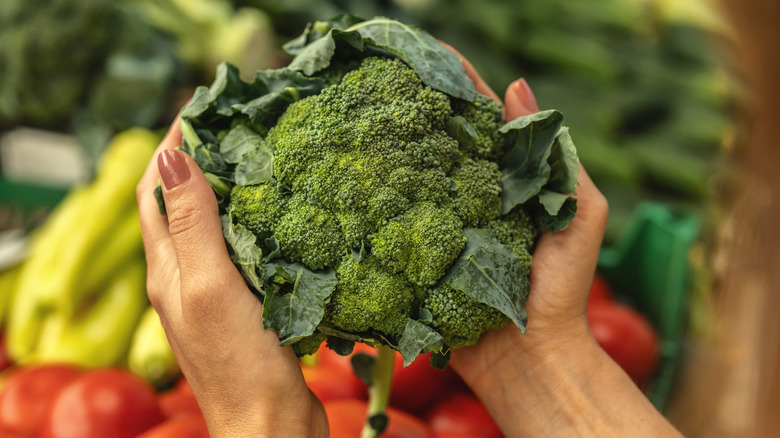 Woman picking up broccoli at the grocery store.