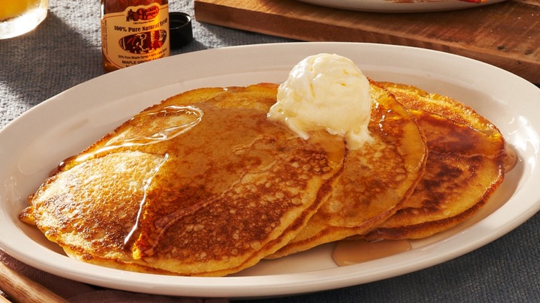 Cracker Barrel pancakes with butter and syrup, and bacon and eggs in background