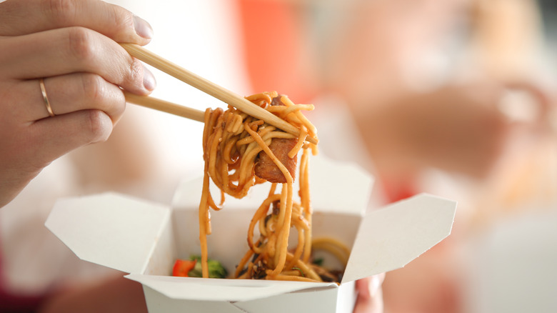 Person holding noodles with disposable chopsticks