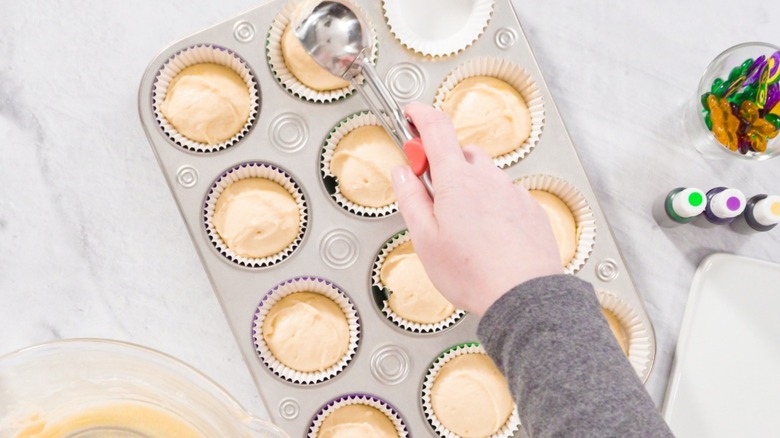 A person scooping cupcake batter into baking cups